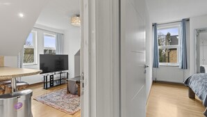 A modern bedroom with a large window, a bed, and a TV in a separate room. - Cosy Flat In London  (London)