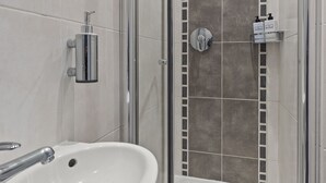A modern bathroom with a white sink, a glass shower enclosure, and a tiled shower wall. - Cosy Flat In London  (London)