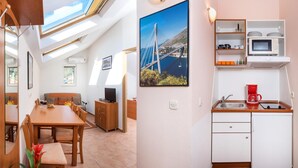 Ett kompakt bostadsutrymme med en matplats, ett litet kök och ett vardagsrum med ett stort fönster som vetter mot en vacker utsikt.