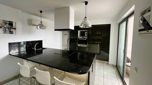 A modern kitchen with a black countertop, stainless steel appliances, and white chairs.