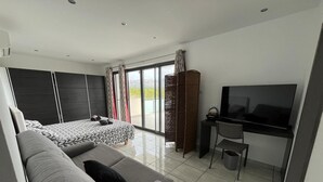 A modern hotel room with a large bed, a sofa, a desk with a TV, and a balcony with curtains.