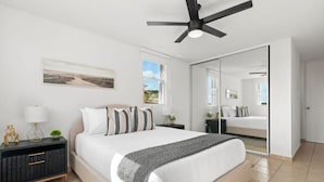 A modern bedroom with a large bed, a ceiling fan, a nightstand with a lamp, and a large mirror. - Victoria Marine’s View | Modern 3BR in Fajardo (Fajardo)