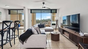 A modern living room with a sofa, a coffee table, a TV, and a balcony with a city view. - Victoria Marine’s View | Modern 3BR in Fajardo (Fajardo)