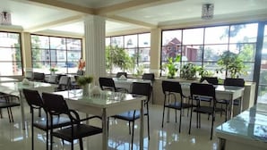 Un vaste espace dédié à la salle à manger, avec de nombreuses tables et chaises, de grandes fenêtres offrant une vue sur l’extérieur et un aménagement intérieur propre et moderne.