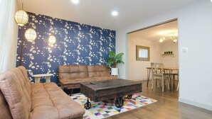Un salon comprenant un canapé, une table basse sur roulettes, un tapis à motifs et un mur orné d’un motif floral.