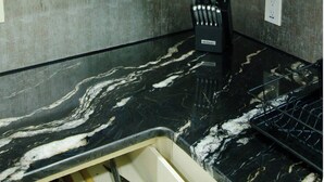 Une cuisine avec des meubles blancs, un plan de travail en marbre noir et un bloc à couteaux.