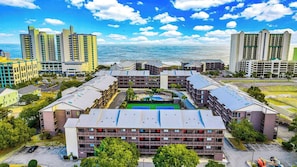 Un hotel de varios pisos con un patio central, rodeado de edificios altos, y vista al mar.