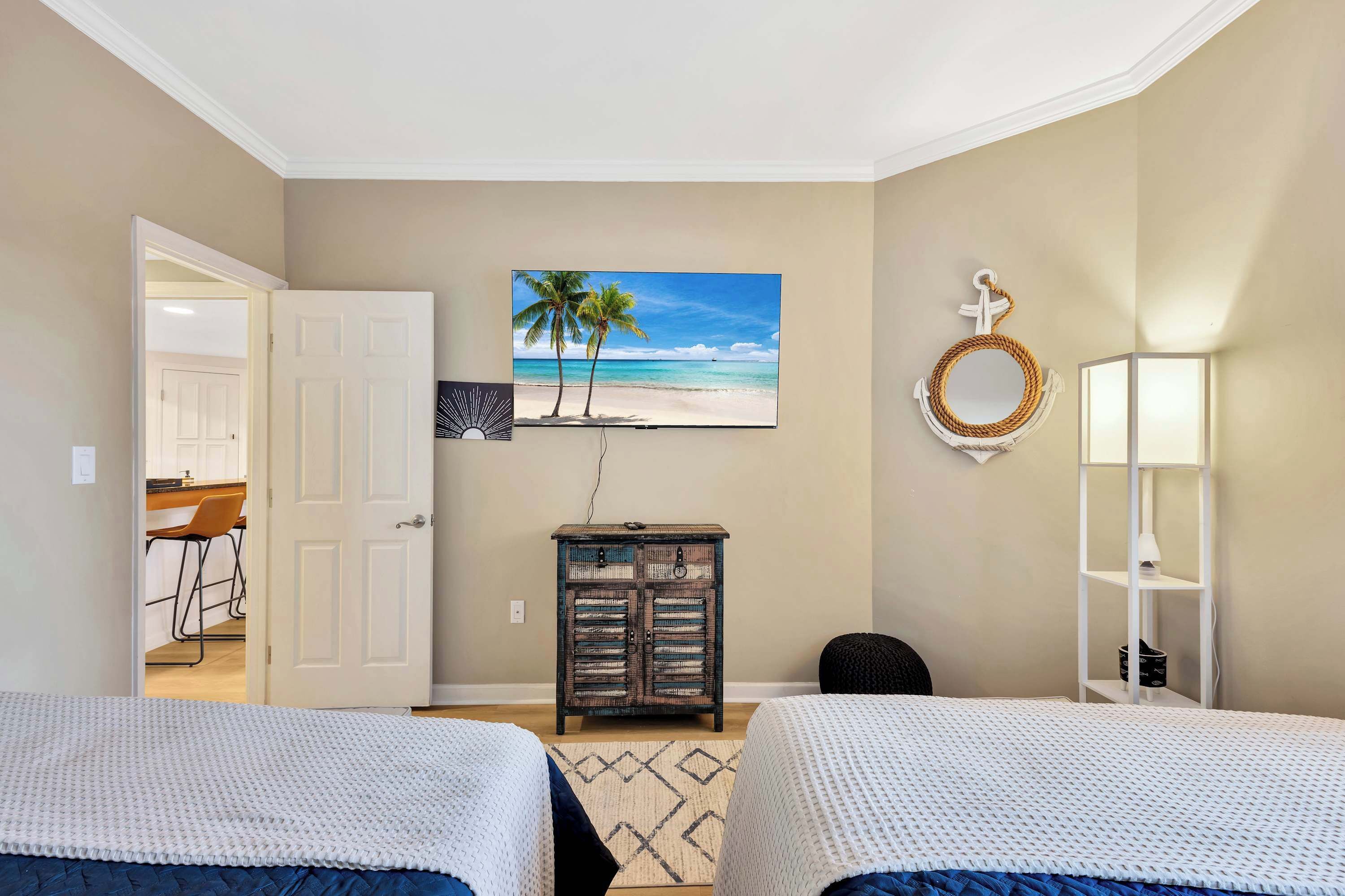 Ein Schlafzimmer mit zwei Betten, einem Strandbild, einer Wanddekoration aus Weidwerk und einem weißen Regal mit einer Lampe.