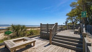 Une terrasse en bois avec des marches menant à un point de vue sur la plage, une table de pique-nique et une poubelle.
