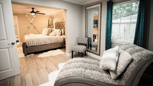 Un dormitorio con cama, una silla, un espejo y un ventilador de techo.