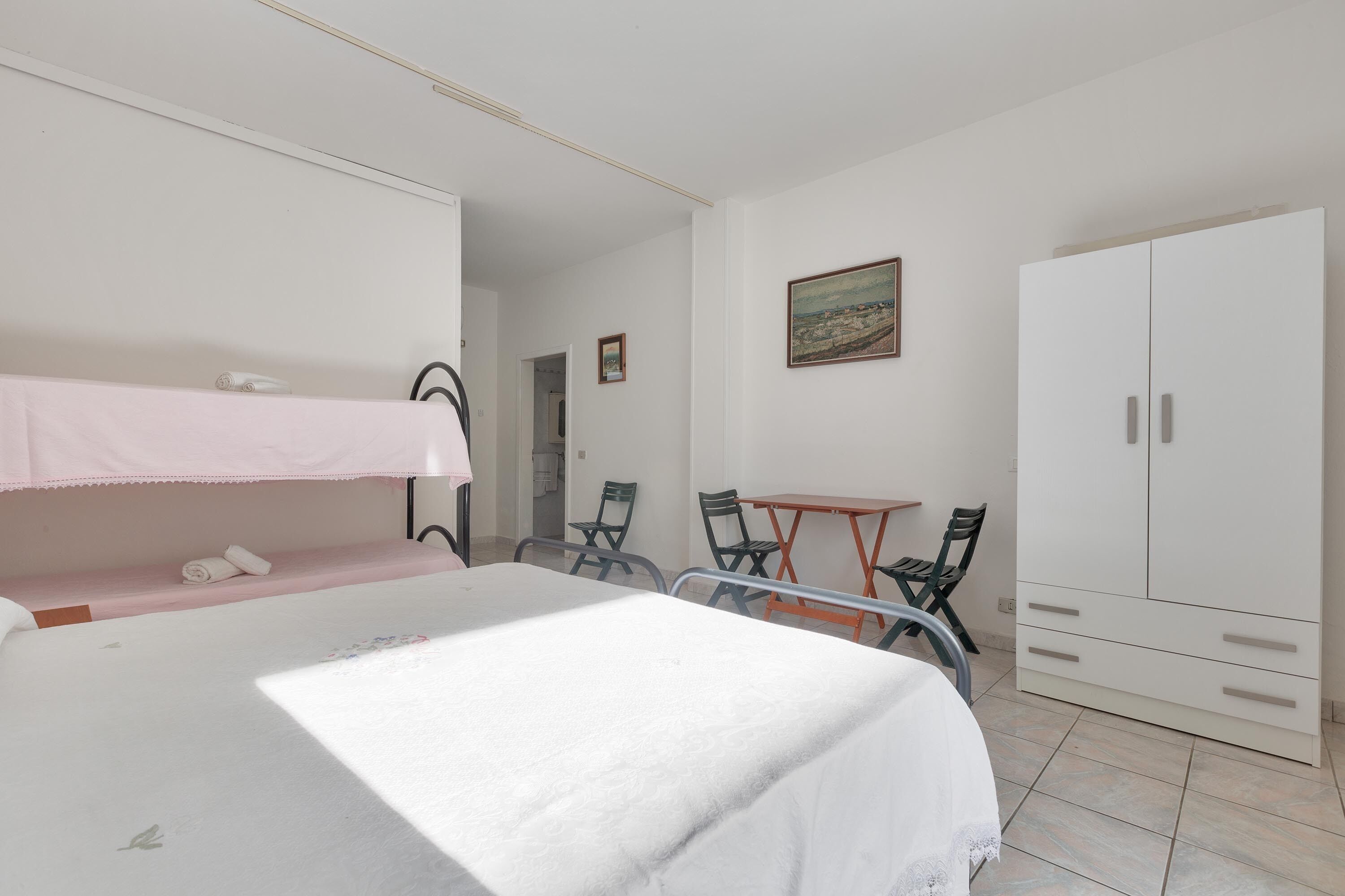 A bedroom with bunk beds, a desk, chairs, and a wardrobe.
