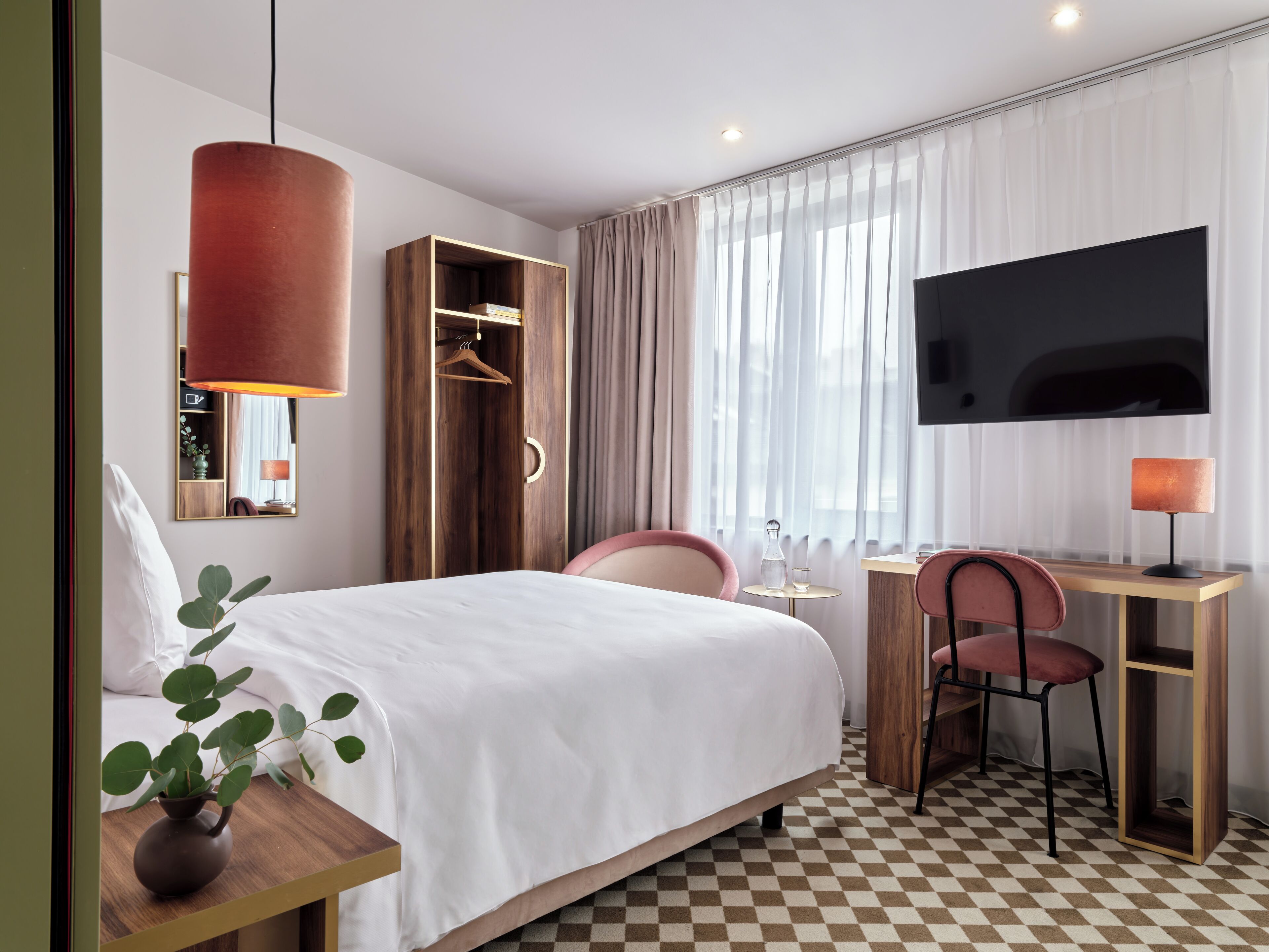 Une chambre d’hôtel équipée d’un lit, d’un bureau, d’une chaise, d’une télévision, d’une armoire et d’une plante.