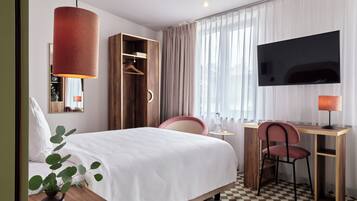Une chambre d’hôtel équipée d’un lit, d’un bureau, d’une chaise, d’une télévision, d’une armoire et d’une plante.
