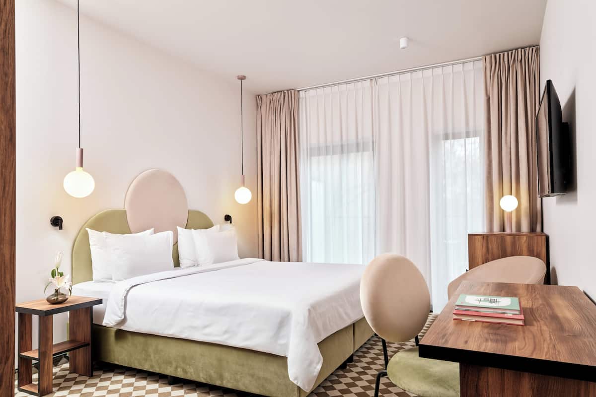A hotel room with a bed, bedside table, chair, and a TV mounted on the wall.