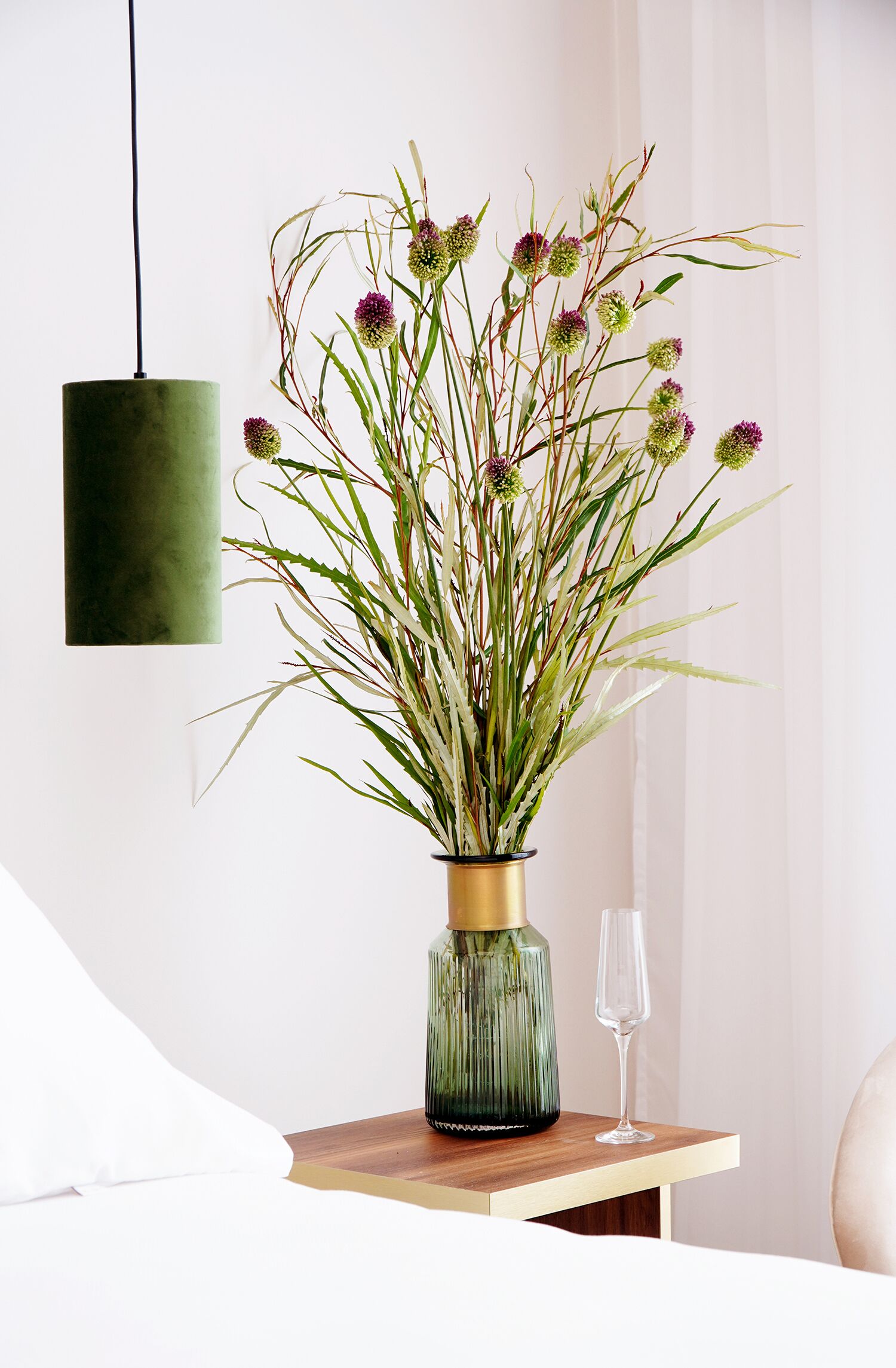 Un jarrón con diseño dorado y verde sobre una mesa de madera, junto a una copa de cristal.