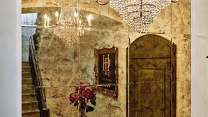Um hall imponente com piso xadrez, um candelabro, uma escadaria e uma porta com uma placa.