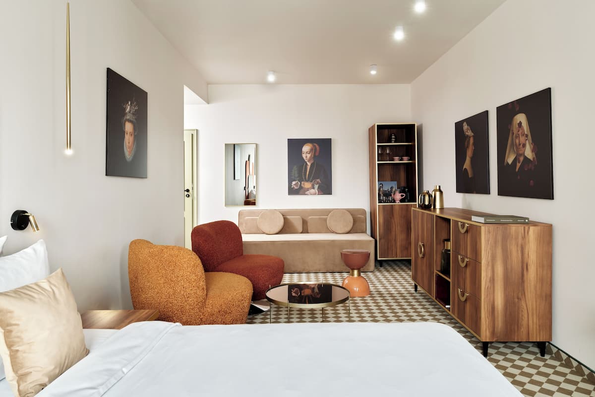 A modern hotel room with a bed, a sofa, a coffee table, and a wooden cabinet.