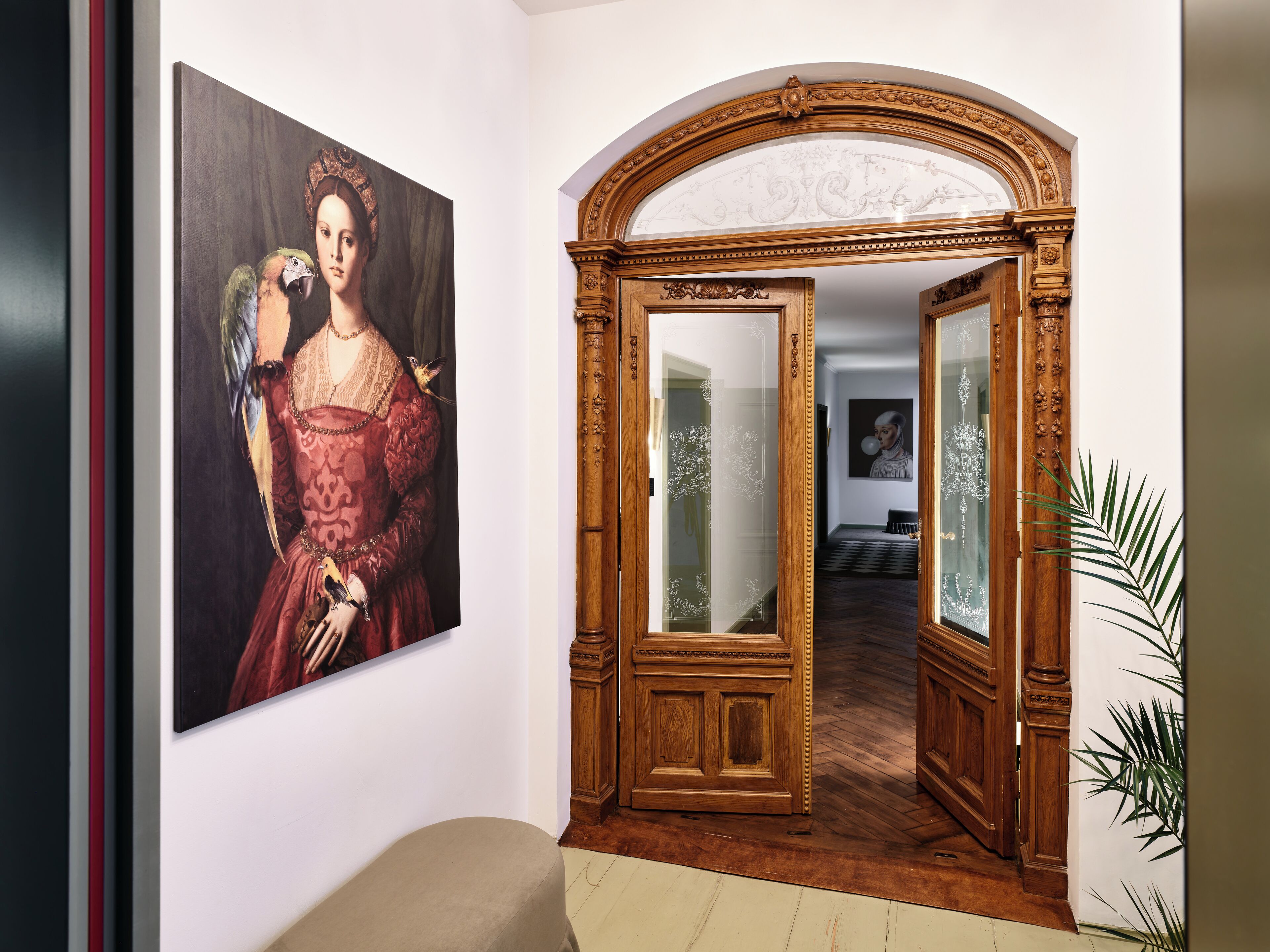 A hallway with a large painting, an ornate wooden door, and a plant.