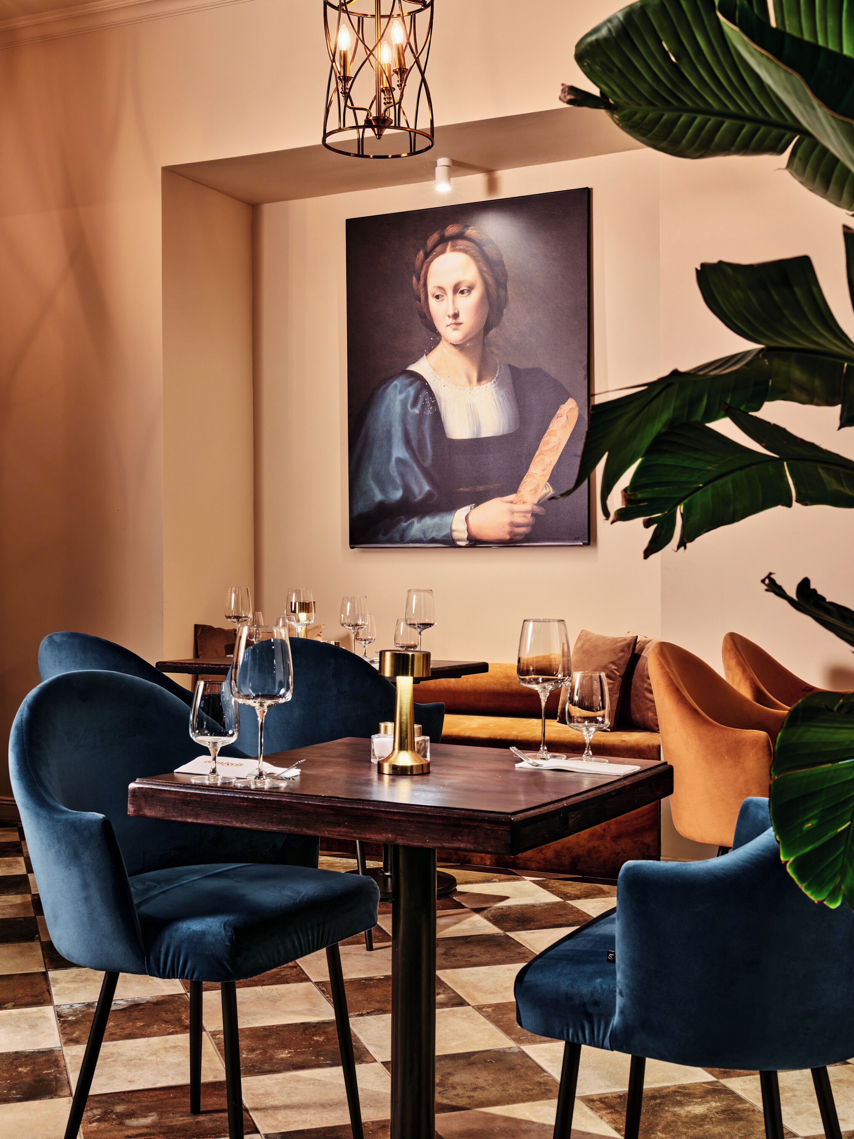 Comedor con suelo a cuadros, una mesa con copas de vino y sillas tapizadas en azul.