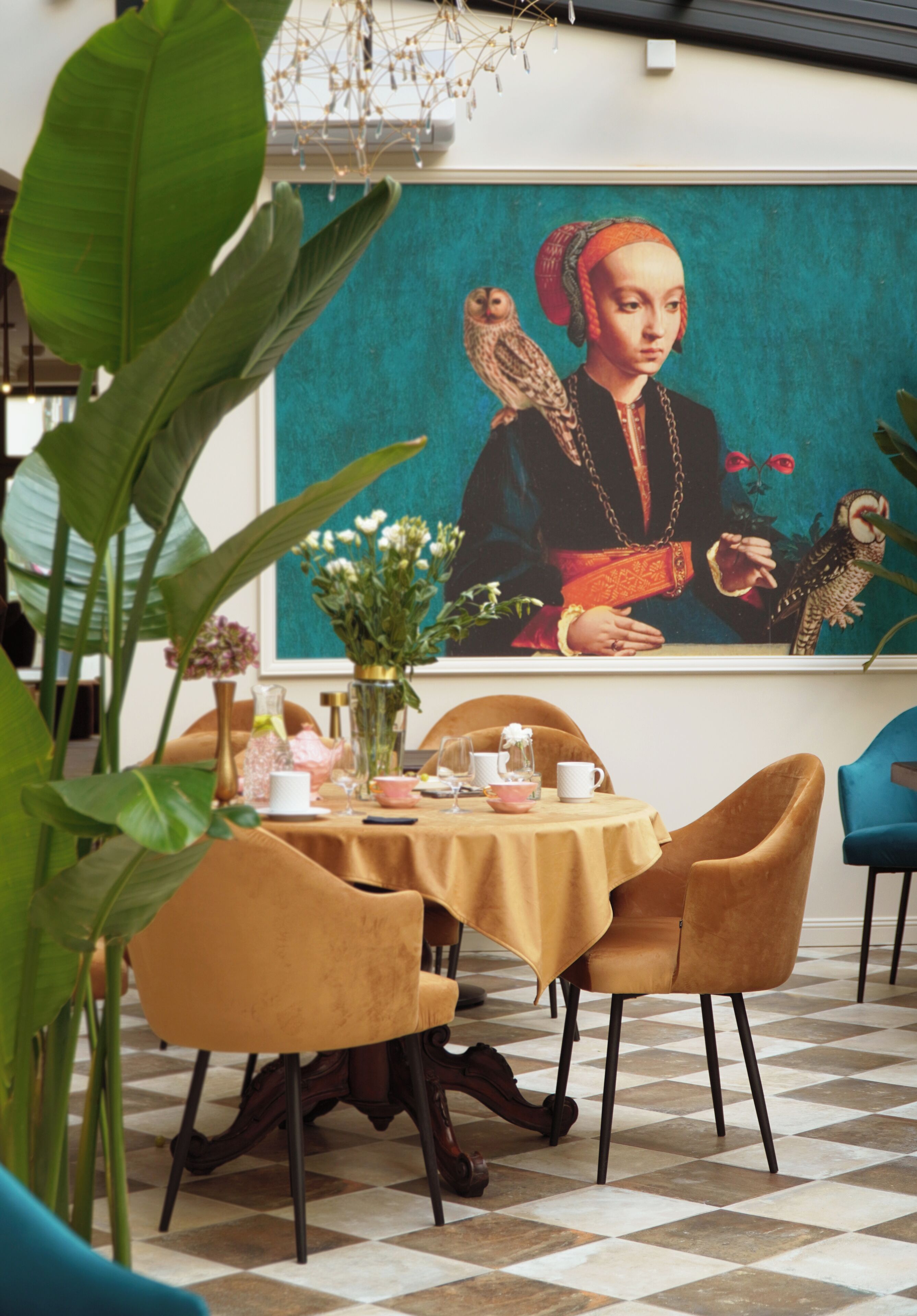 A dining area with a table set for two, a large painting on the wall, and a checkered floor.