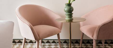 A room with two pink chairs, a round table with a green vase, and a checkered floor.