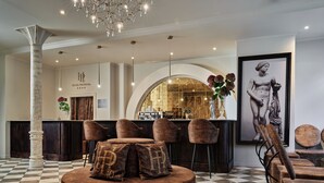 Um lobby com piso xadrez, assentos redondos, balcão de recepção e área de bar.