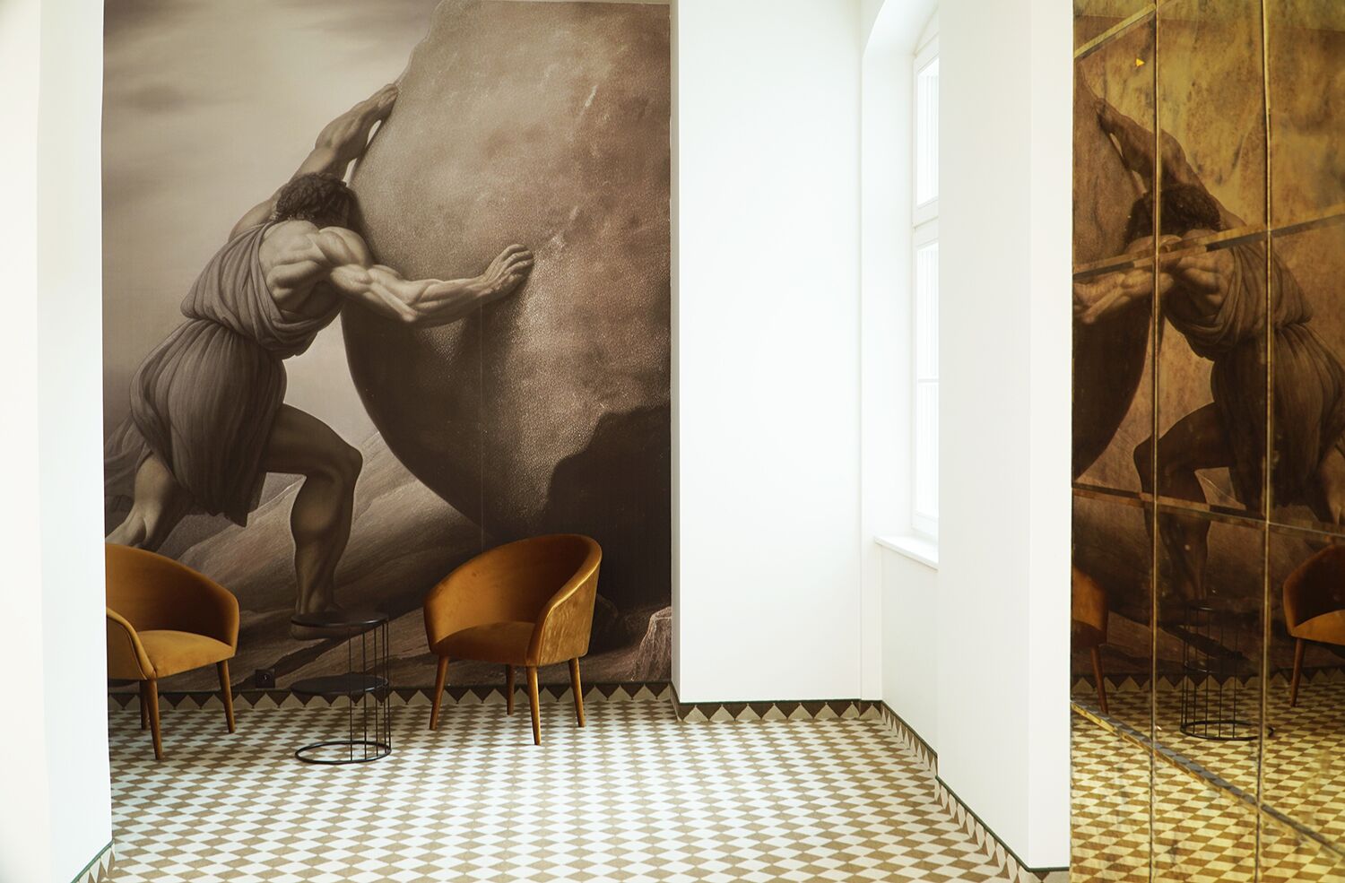 Una habitación con un mural grande de una figura musculosa escalando una roca, dos sillas de madera y un piso a cuadros.