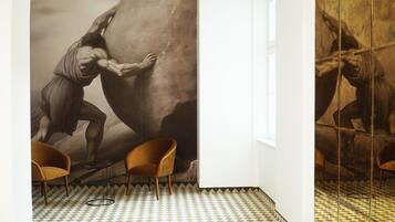 Una habitación con un mural grande de una figura musculosa escalando una roca, dos sillas de madera y un piso a cuadros.