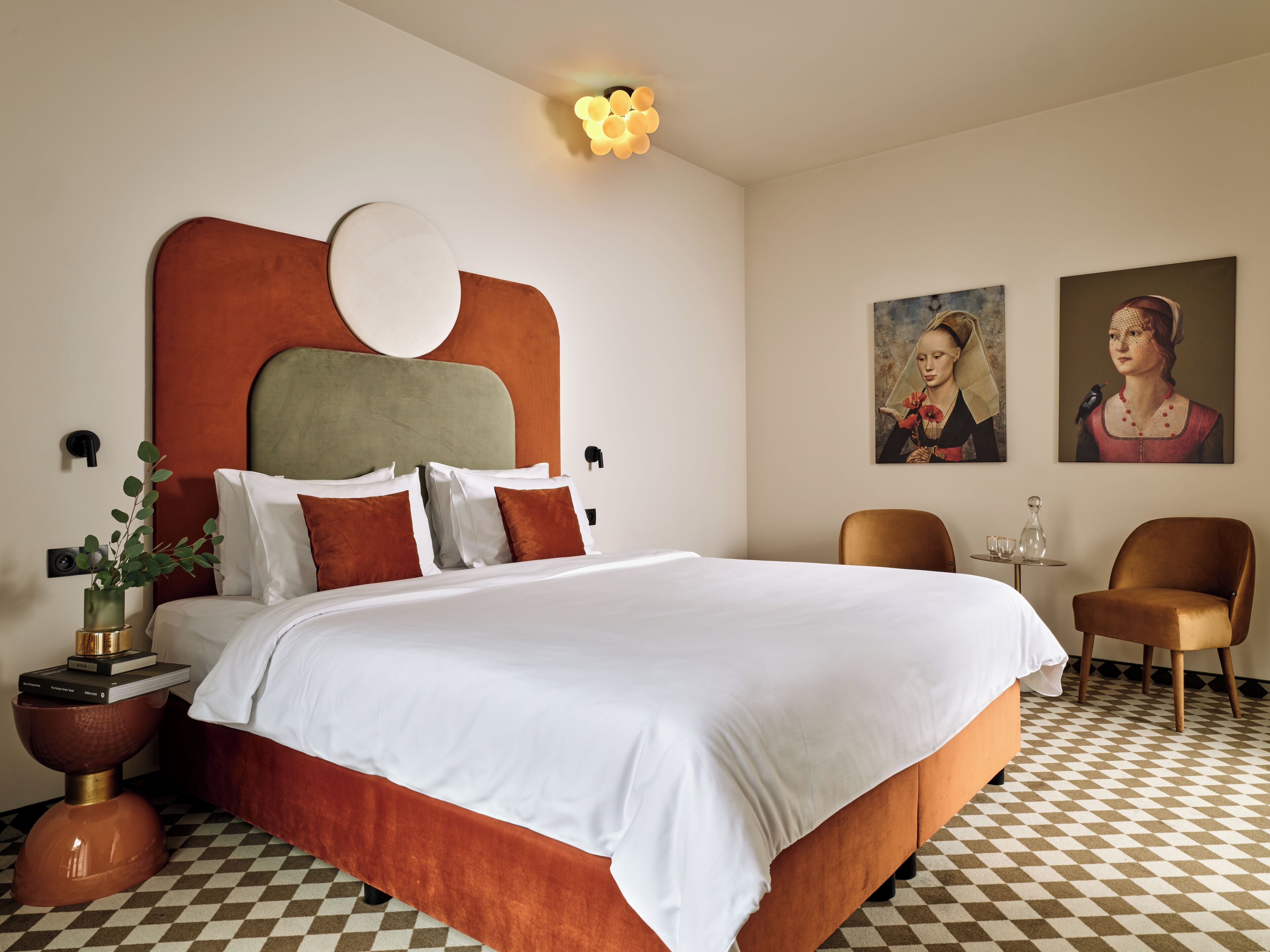 A modern hotel room with a large bed, two chairs, a small table, and artwork on the walls.