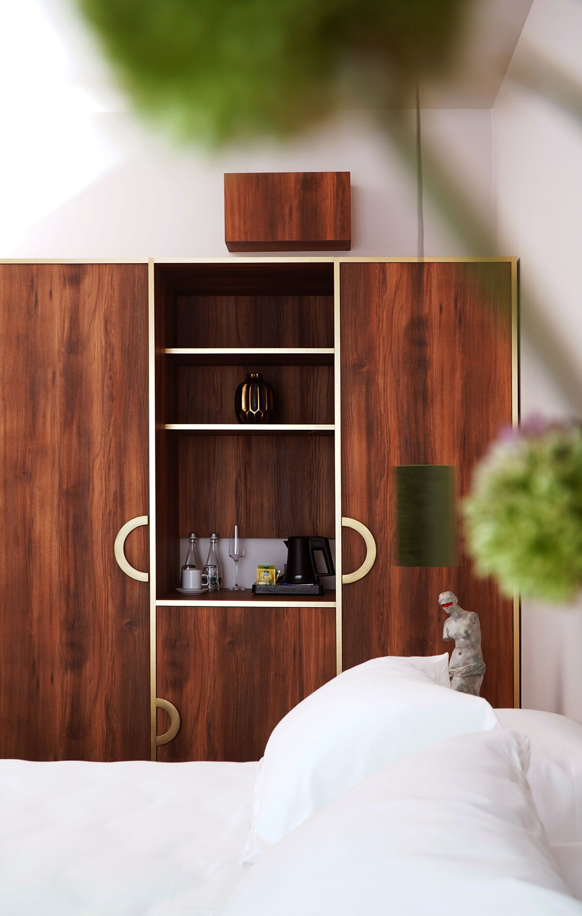 A bedroom with a wooden wardrobe, a bed, and a statue.