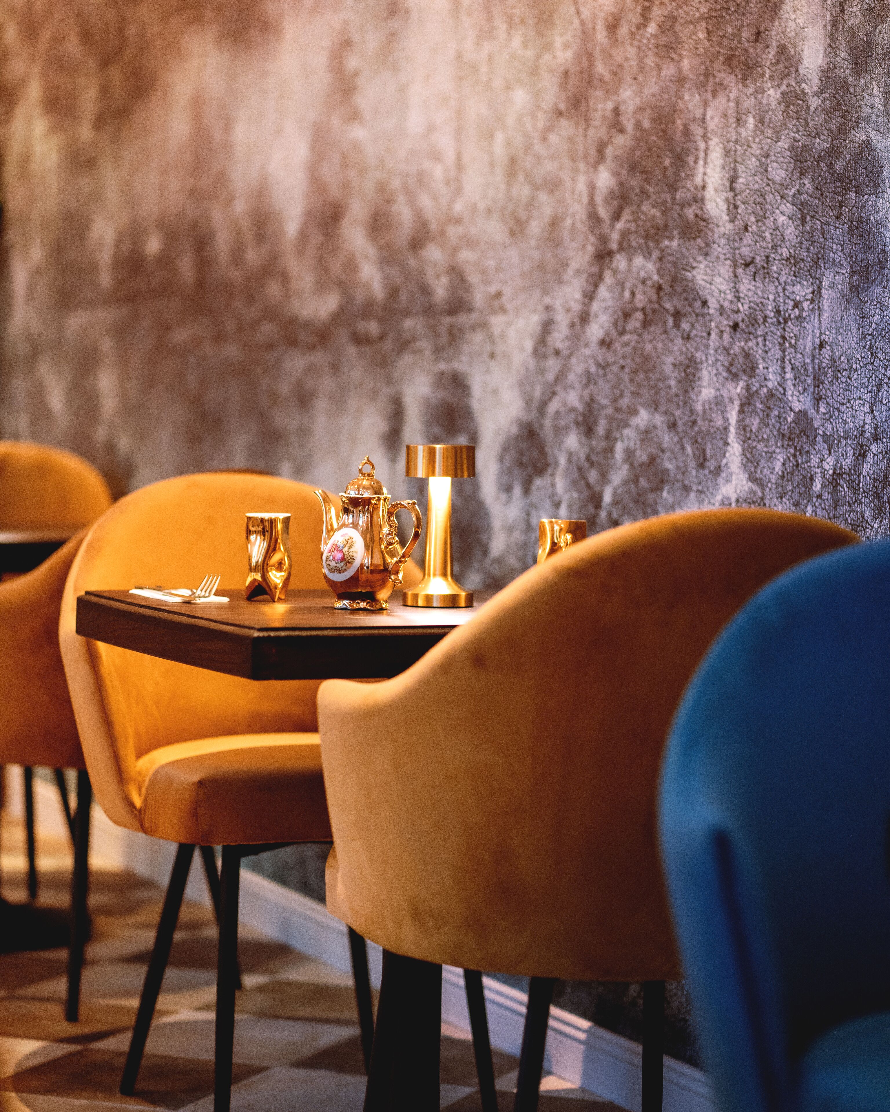 A dining area with a table set for two, featuring a gold teapot, cups, and a lamp.