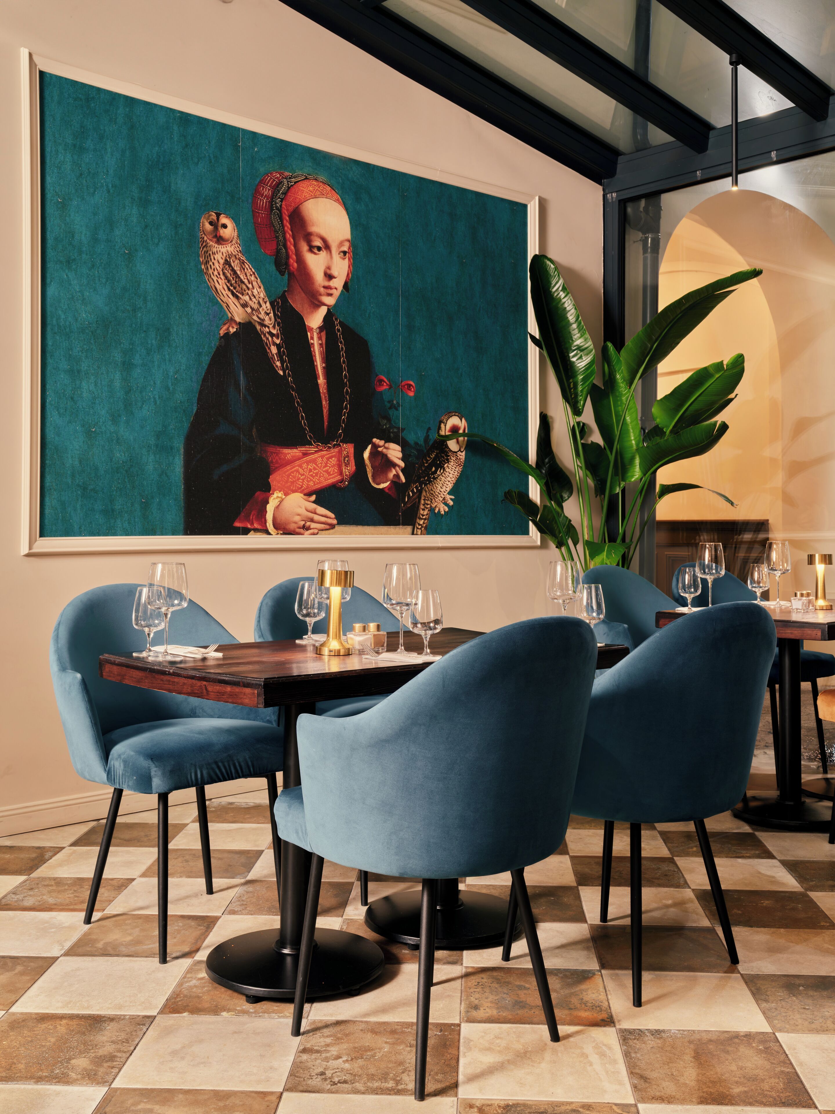 A dining area with a table set for four, blue chairs, and a large painting on the wall.