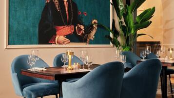A dining area with a table set for four, blue chairs, and a large painting on the wall.