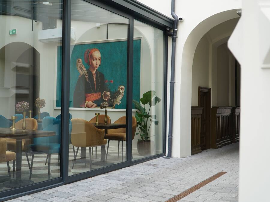 A modern interior with a dining area, a large window with a painting, and a hallway with a potted plant.