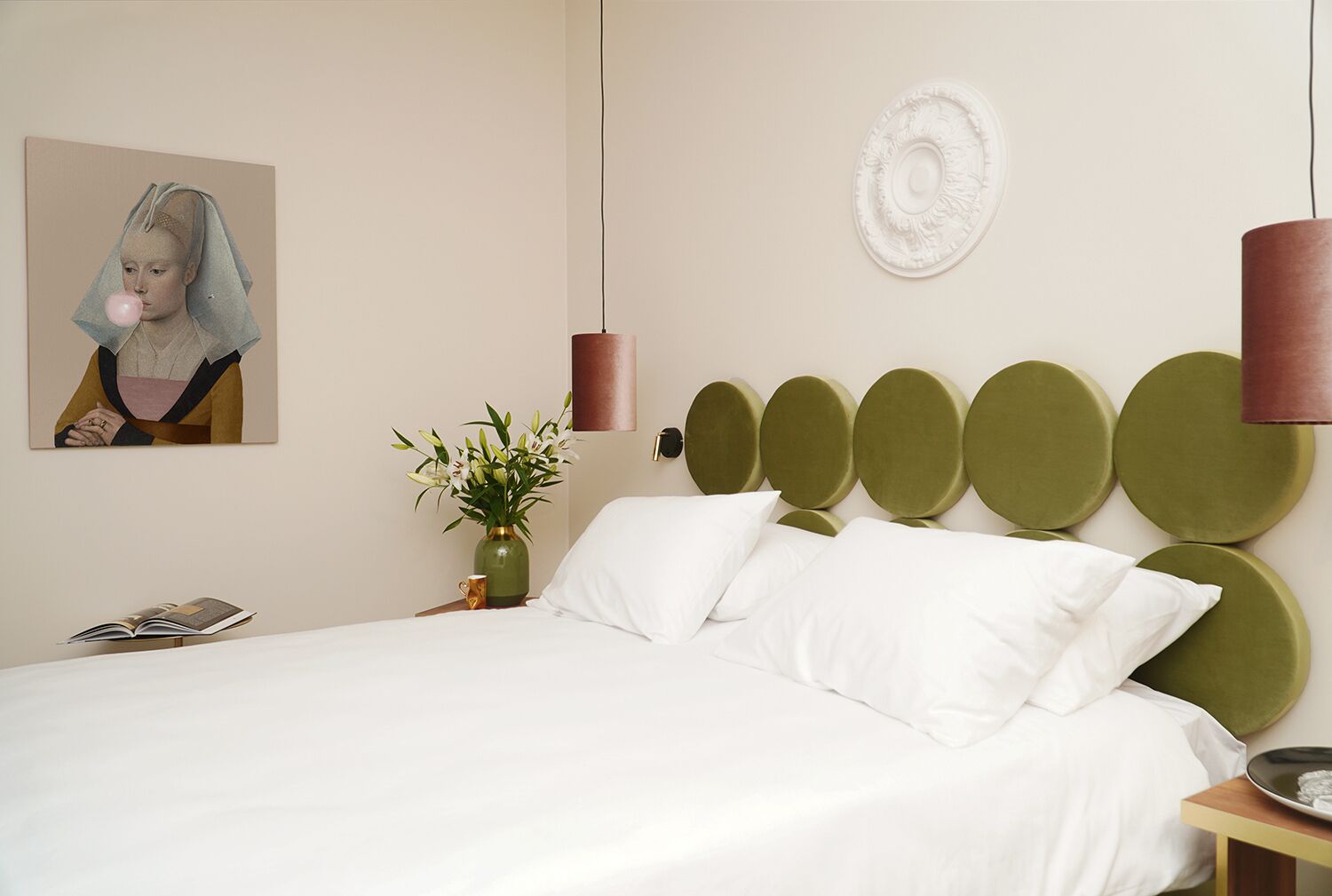 Un dormitorio moderno con una cama grande, un cabecero verde, un jarrón con flores y un cuadro en la pared.