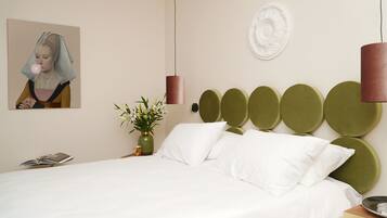 Un dormitorio moderno con una cama grande, un cabecero verde, un jarrón con flores y un cuadro en la pared.