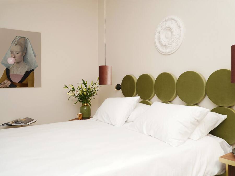 Un dormitorio moderno con una cama grande, un cabecero verde, un jarrón con flores y un cuadro en la pared.