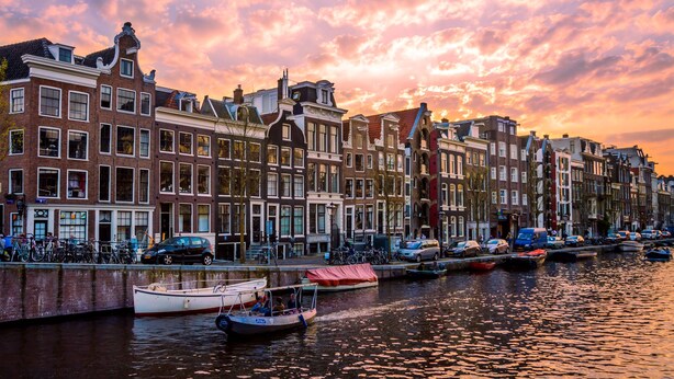 Un canal flanqueado por edificios históricos, con barcos amarrados a lo largo del agua y un cielo al atardecer.