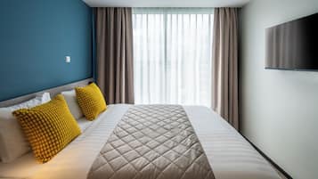 Een moderne hotelkamer met een groot bed, twee kussens, een flatscreen televisie en een raam met gordijnen.
