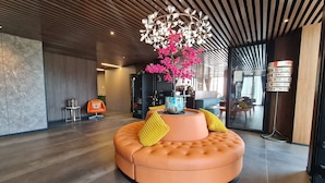 Un vestíbulo moderno con una zona de estar circular naranja, un arreglo floral rosa decorativo y una lámpara de techo original.