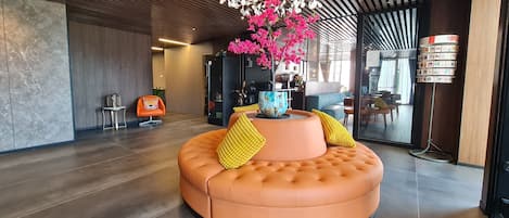 A modern lobby with a circular orange seating area, a decorative pink flower arrangement, and a unique ceiling light fixture.