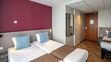 A hotel room with two beds, a wooden floor, a red accent wall, and a mirror.