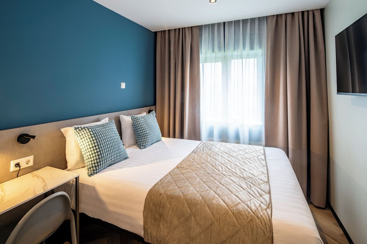 A hotel room with a bed, a desk, and a TV.