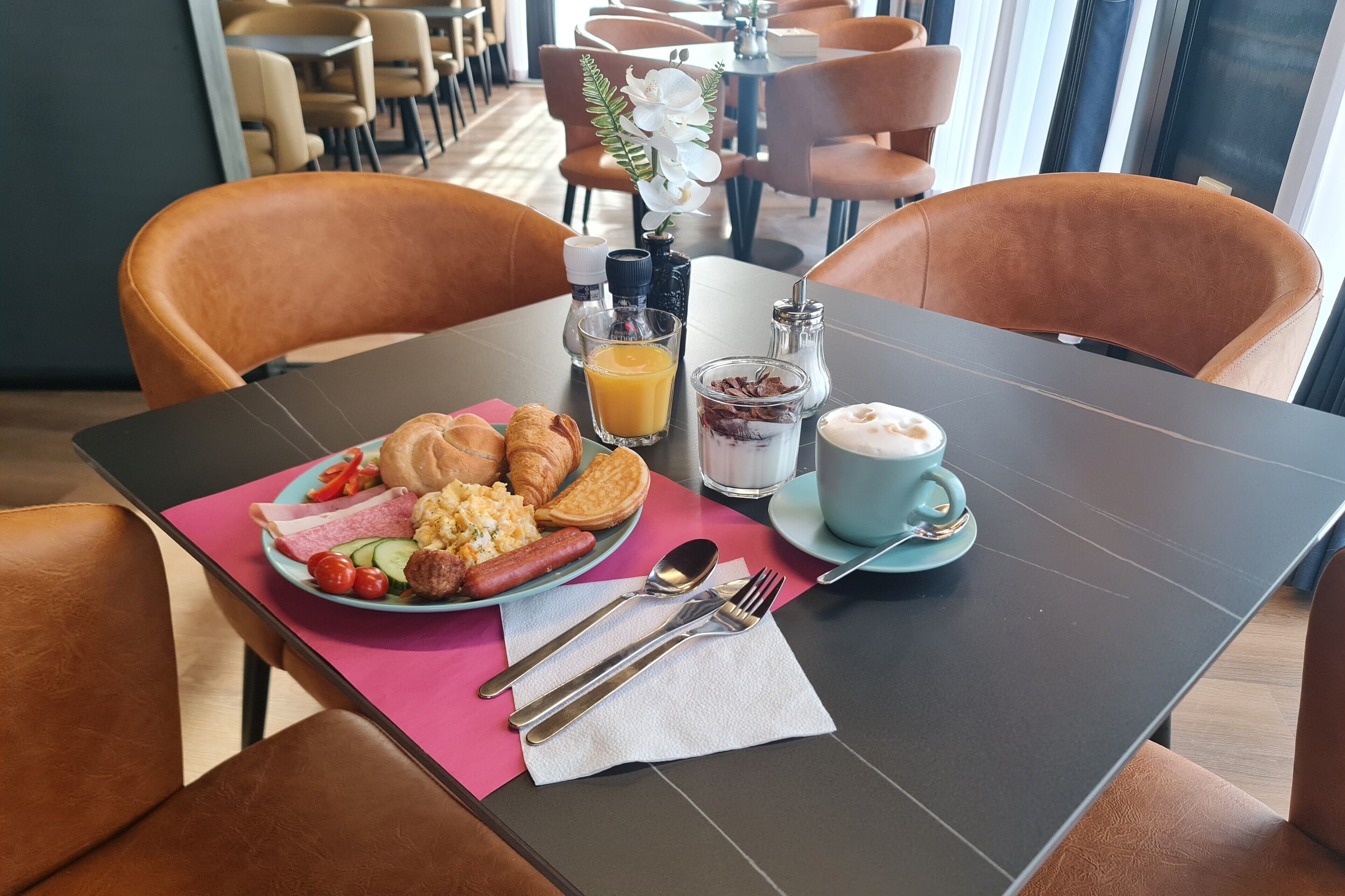 A breakfast table with croissants, sausages, eggs, and a cup of coffee in a hotel setting.
