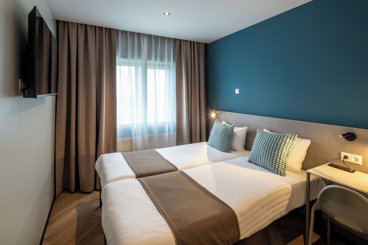A hotel room with two beds, a desk, and a TV.