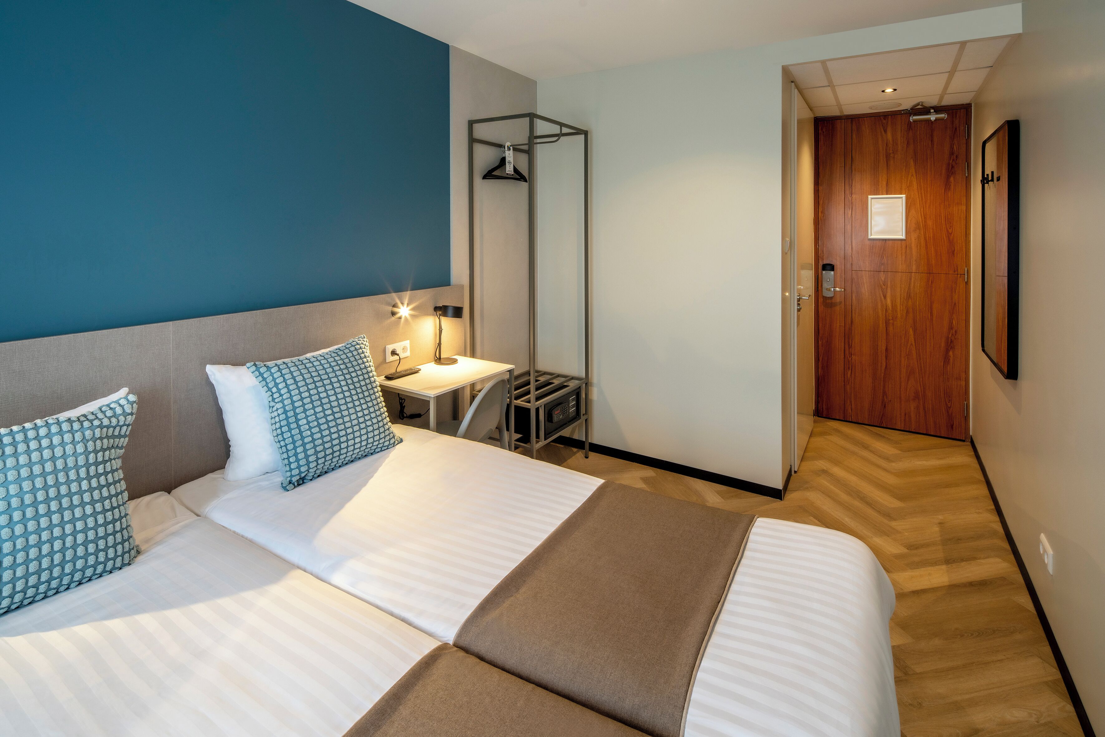 Une chambre d’hôtel avec deux lits, un bureau, un miroir et une porte en bois.