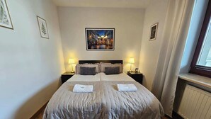 A bedroom with a large bed, two bedside tables with lamps, a framed picture on the wall, and a window with curtains. - Spacious Apartment | Balcony, Parking, Pool (Kraków)
