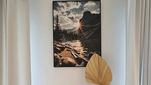 A framed landscape painting of a mountainous sunset, a wooden vase with a fan, and a small black container on a wooden table. - Spacious Apartment | Balcony, Parking, Pool (Kraków)