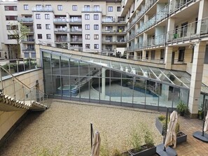 Un atrio de varios niveles con barandillas de vidrio, una escalera central y un patio empedrado.