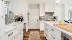 Una cocina moderna con armarios blancos, una isla central, horno empotrado y una estación para café.